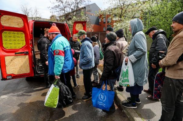People wait in a line to collect humanitarian food aid following the Russian shelling attack in Kherson on April 19, 2023.