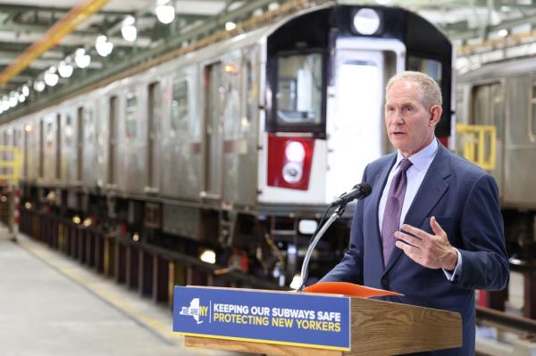 An MTA official is pictured speaking at a podium in front of a train.
