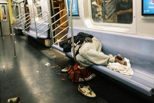 A man is seen sleeping on a subway car bench.