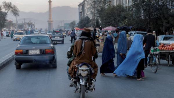 A group of women wearing burqas crosses the street as members of the Taliban drive past in Kabul, Afghanistan October 9, 2021. REUTERS/Jorge Silva/File Photo