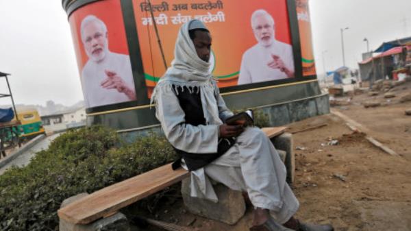  A Muslim man reads the Koran as he sits in front of a billboard featuring India's Prime Minister Narendra Modi in New Delhi January 20, 2015. REUTERS/Adnan Abidi/File Photo