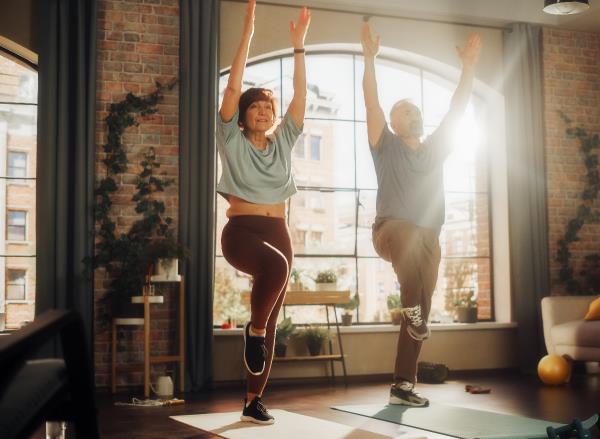 older couple demo<em></em>nstrating exercises for seniors to prevent falls, balancing on yoga mats in apartment
