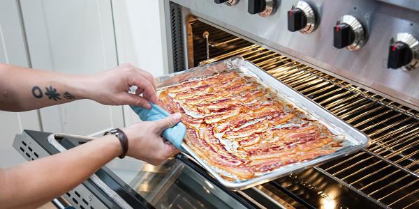 Person removing tray of bacon from co<em></em>nvection oven