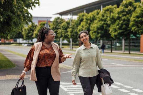 A three quarter length shot of two businesswomen walking and talking to each other after work. They are both dressed smartly and casually and are walking over a road. They are ba<em></em>sed in the North East of England.