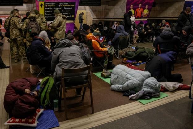 Dozens of people in heavy coats, as well as military perso<em></em>nnel in camouflage gear, huddle at an indoor location.