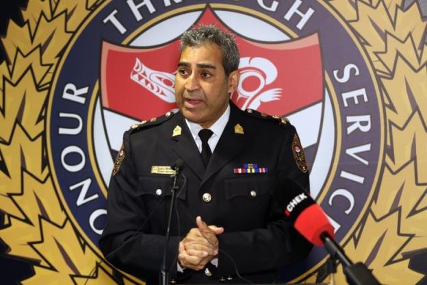 A man in a police uniform stands before a podium speaking with his hands clasped together. Behind him on a screen are the words 'Ho<em></em>nour through service.' 