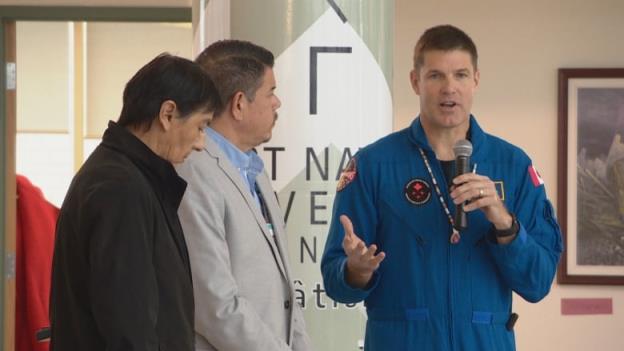Two Indigenous men from Turtle Lodge stand next to astro<em></em>naut Jeremy Hansen, who is holding a microphone.