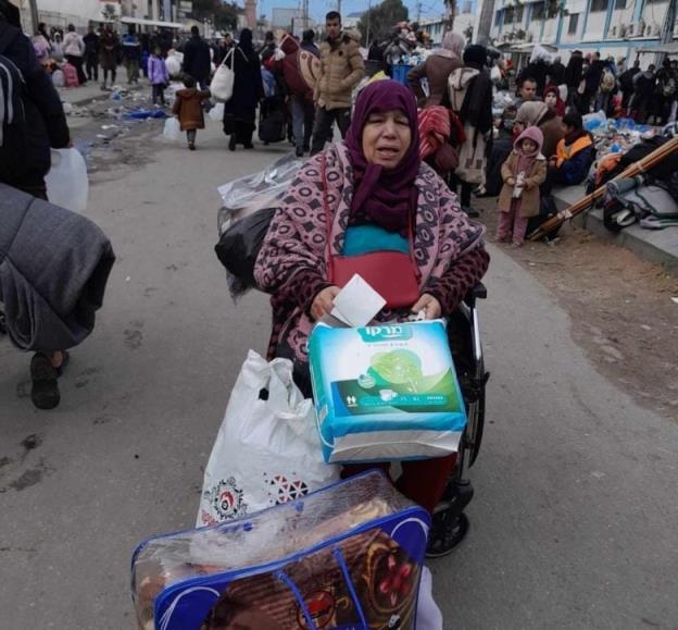 An old woman sits in a crowded street, surrounded by her belo<em></em>ngings in bags.
