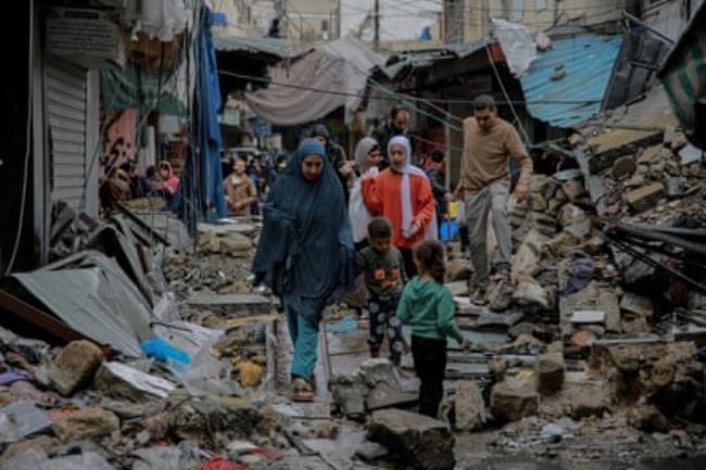 A group of women and children walk between bombed out buildings