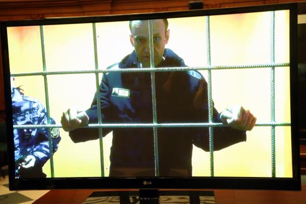 A middle-aged man stands holding the bars of a cage.
