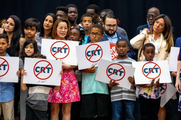 Kids holding signs against Critical Race Theory stand on stage near Florida Gov. Ron DeSantis