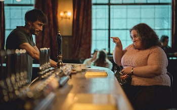 Gadd stands behind a bar replete with beer taps, with Gunning sitting opposite him and gesticulating