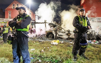 Officers surround the extinguished bus wreckage, which still smokes
