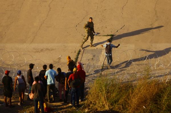 A member of the Texas Natio<em></em>nal Guard tries to inhibit the crossing of a migrant into the United States.