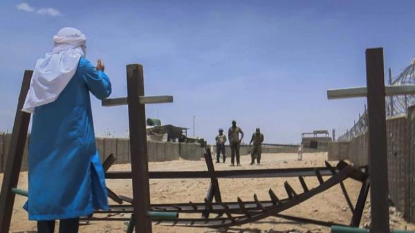 Feras stands at the gate of a UN ba<em></em>se speaking to some people inside