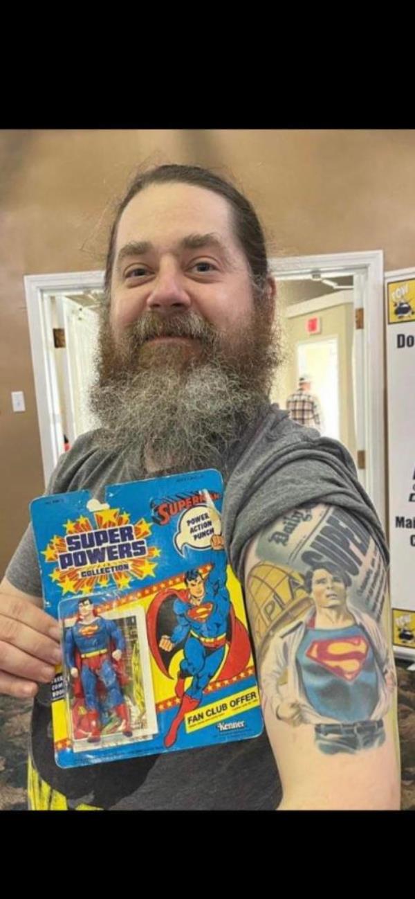 Peyton Brewer-Ross shows off Superman tattoo with superman action figure held next to it.