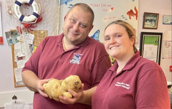 Roni Gill, 23 and Alexander Povalyaev, 42, with the giant potato in Archie's Fish and Chip Shop in Minster in Thanet, September 4th 2023. See SWNS story SWSMpotato. A chippy in Kent has discovered what they reckon could be the UK's biggest spud. Archie's Fish and Chip Shop in Minster in Thanet took to social media to show off the whopper of a potato - that they say has a resemblance to a seal or hippo. Wife and husband owners Natalia Sidorova, 50, and Alexander Povalyaev, 42 posted the video on social media featuring colleague Roni Gill, 23, with the famed veg. The potato's weight is being kept a secret as the chippy intends to host a guessing game for customers - but co<em></em>nfirmed the spud is 10 inches by 6 inches.