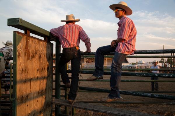 Two cowboys sitting on a fence next to a corral 