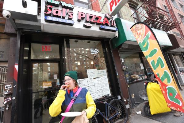 A loyal New Yorker chows down on a slice of authentic NYC pizza outside of Sal's Pizzeria on East 14th Street