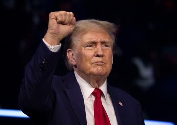 Former President Do<em></em>nald Trump walking o<em></em>nto stage at Turning Point Co<em></em>nvention in Detroit, Michigan, holding up his fist