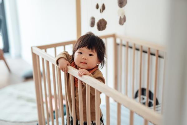 Smiling Asian baby girl standing in cot