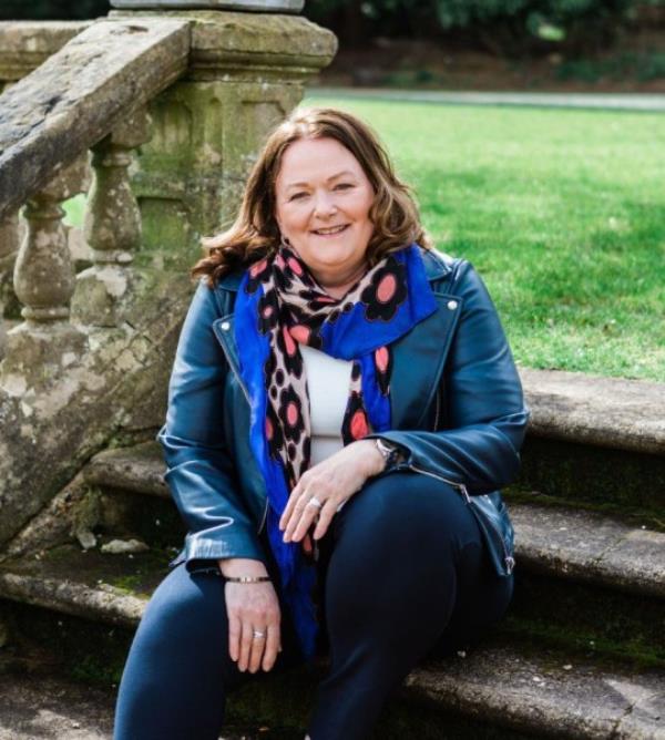 Alison Rios McCrone sitting outside on stone steps next to a stone balustrade, with grass behind her