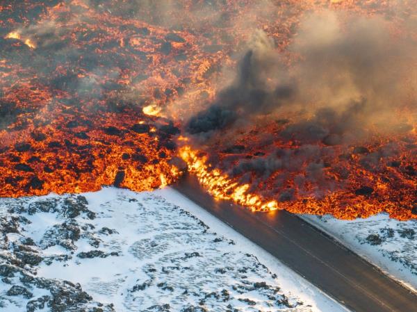 Lava flowing on a road with smoke and steam rising in the air, caused by a volcanic eruption in Iceland, Feb. 8, 2024.