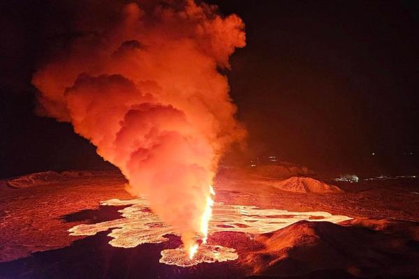 A volcanic eruption in Iceland: billowing smoke and flowing lava pouring out of a new fissure.