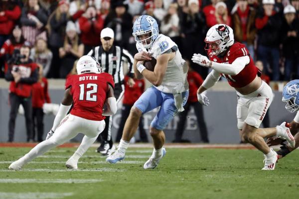 North Carolina's Drake Maye tries to run the ball between North Carolina State defensive back Devan Boykin and linebacker Payton Wilson (11) during the first half in Raleigh, N.C., on Nov. 25, 2023. 