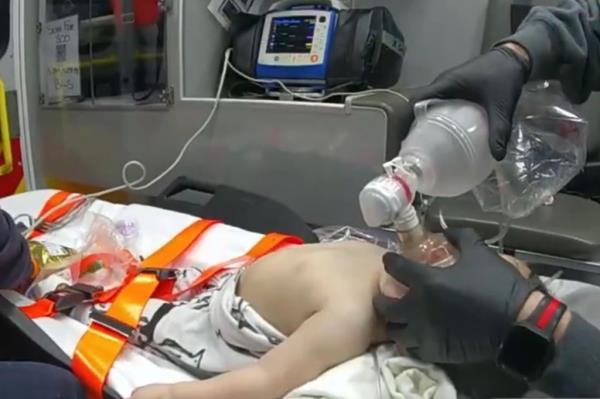 Medic places oxygen mask over baby boy's face in back of ambulance 