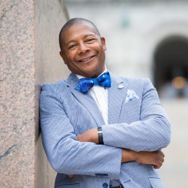 State Sen. James Sanders, Jr. leaning against a marble wall in front of a blurry background outside. 