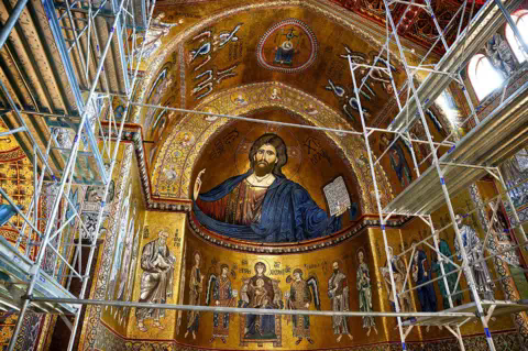Reuters The apse of Monreale's cathedral in Sicily, showing a detailed mosaic of Christ and other religious symbology in mostly gold, with scaffolding in the foreground.